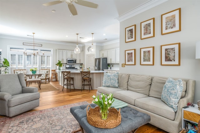 living area featuring recessed lighting, light wood-type flooring, ornamental molding, and ceiling fan with notable chandelier