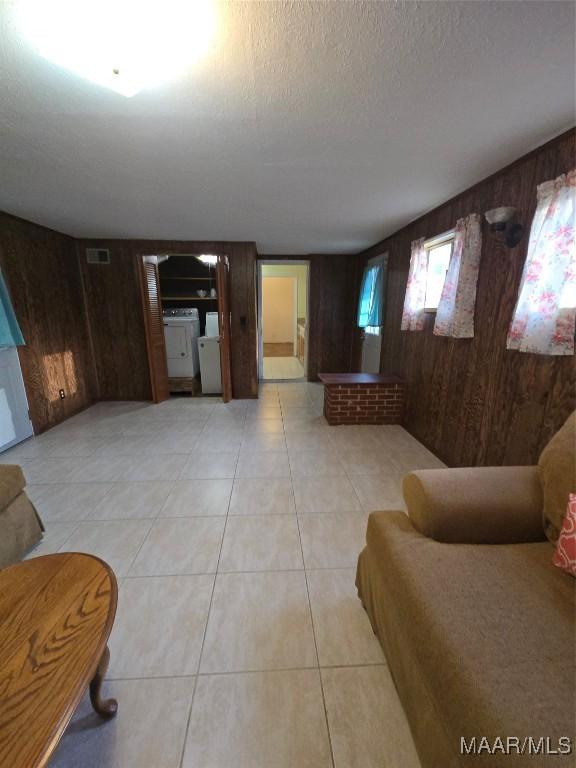 living area with visible vents, independent washer and dryer, a textured ceiling, wood walls, and light tile patterned floors