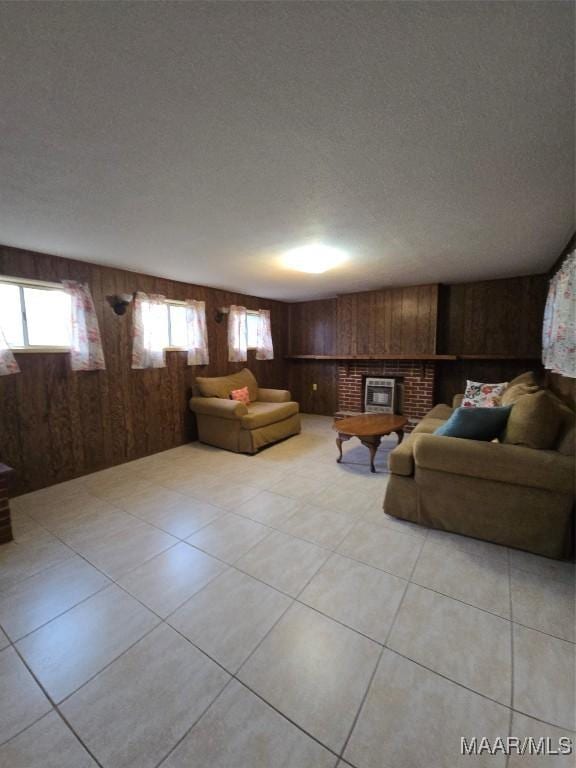 living room with light tile patterned floors, wooden walls, a brick fireplace, and a textured ceiling