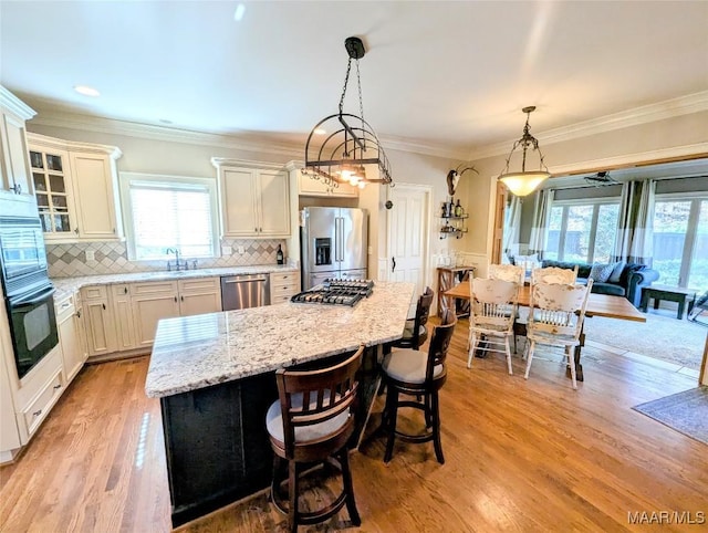 kitchen featuring a kitchen island, light wood-type flooring, light stone counters, appliances with stainless steel finishes, and a sink