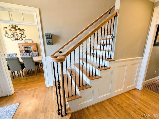 stairway with a decorative wall, an inviting chandelier, and wood finished floors