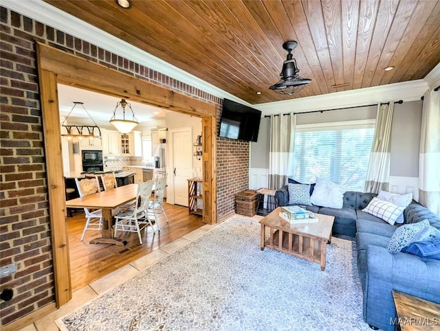 living room with a wainscoted wall, brick wall, crown molding, light tile patterned floors, and wood ceiling