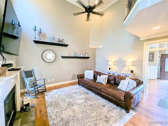 living area featuring wood finished floors, baseboards, a high ceiling, a fireplace, and ceiling fan