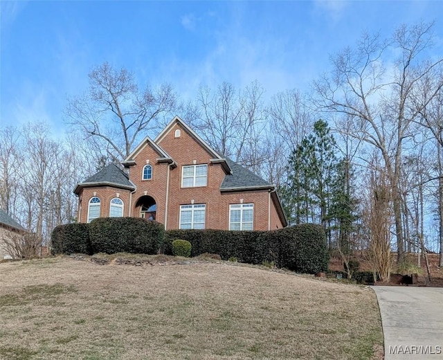 view of front of property with brick siding, a front lawn, and a shingled roof