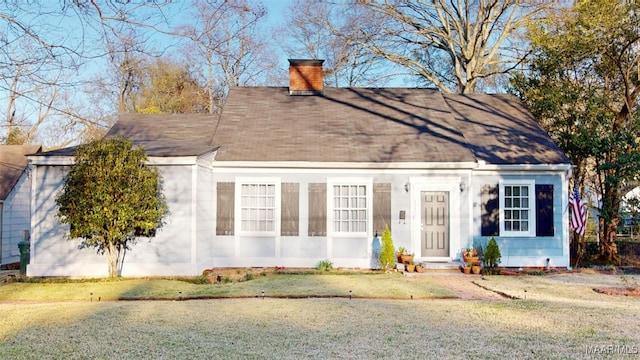 view of front facade featuring a front lawn, roof with shingles, and a chimney