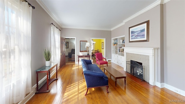 living area featuring built in shelves, baseboards, light wood finished floors, a fireplace, and crown molding