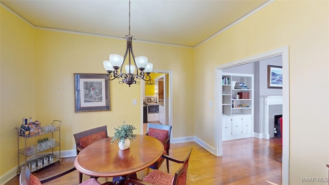 dining room featuring baseboards, light wood-style floors, a chandelier, and crown molding