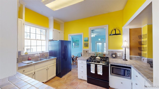 kitchen featuring tile countertops, black appliances, white cabinets, and a sink