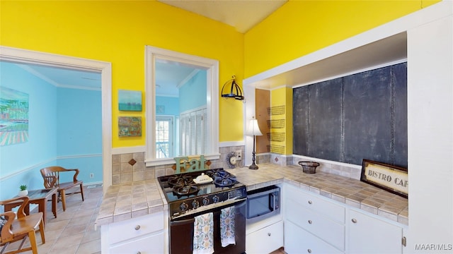 kitchen with gas stove, stainless steel microwave, white cabinets, and tile countertops