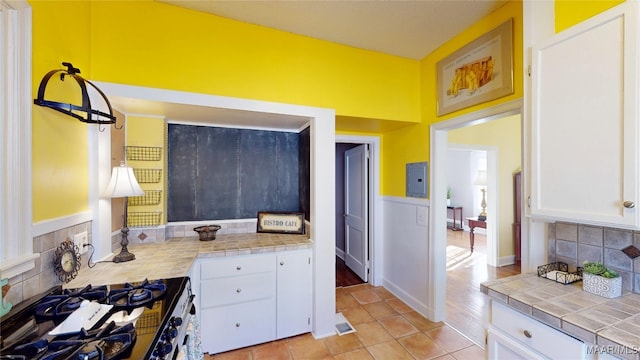 kitchen featuring tile countertops, visible vents, stainless steel gas stove, white cabinetry, and tasteful backsplash