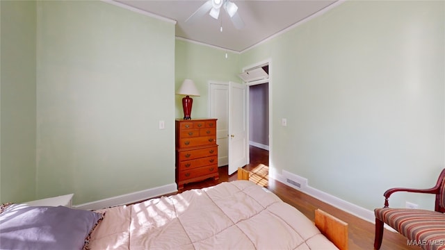 bedroom with visible vents, wood finished floors, a wall unit AC, crown molding, and baseboards