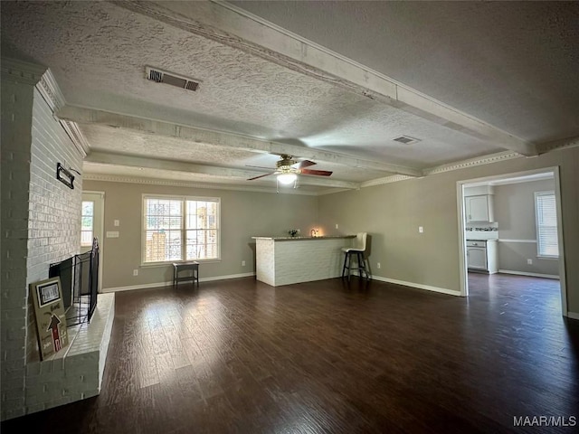 unfurnished living room with visible vents, beam ceiling, dark wood-type flooring, a textured ceiling, and a brick fireplace