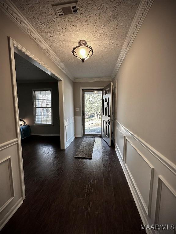 entryway with visible vents, ornamental molding, a decorative wall, a textured ceiling, and dark wood-style flooring