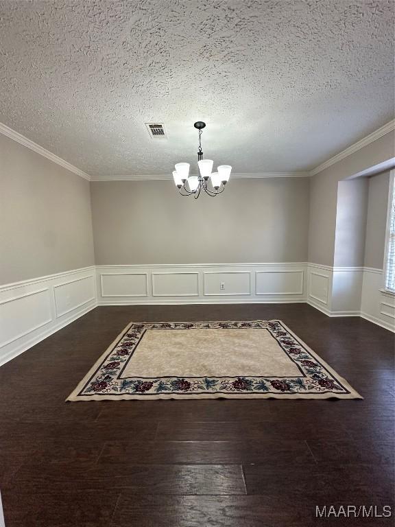 unfurnished dining area with visible vents, dark wood finished floors, an inviting chandelier, ornamental molding, and a textured ceiling