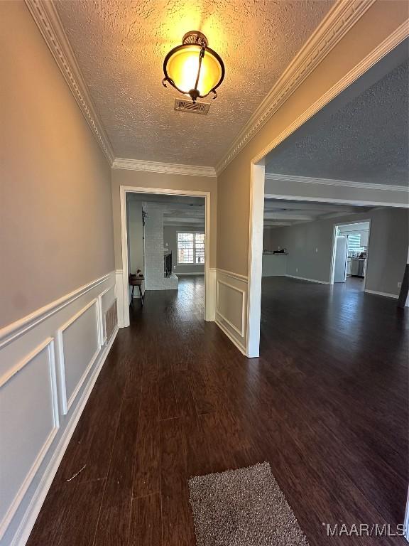 hall with visible vents, ornamental molding, a textured ceiling, wood finished floors, and a decorative wall