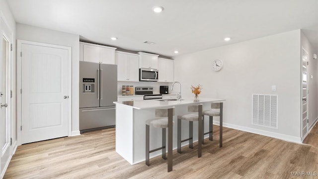 3140 Knotts Dr, Montgomery, AL 36116 - kitchen with appliances with stainless steel finishes, a breakfast bar area, light wood-style flooring, an island with sink, and white cabinetry