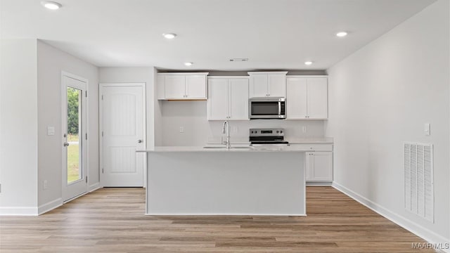 3140 Knotts Dr, Montgomery, AL 36116 - kitchen featuring stainless steel microwave, electric stove, white cabinets, a center island with sink, and light wood finished floors