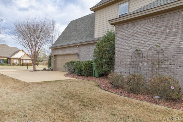 view of home's exterior featuring a lawn, concrete driveway, a shingled roof, a garage, and brick siding