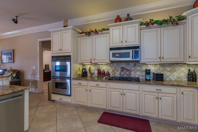 kitchen with tasteful backsplash, crown molding, dark stone countertops, light tile patterned flooring, and stainless steel appliances