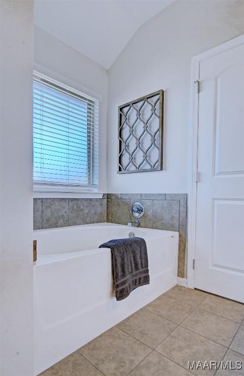 full bath featuring tile patterned floors, lofted ceiling, and a garden tub