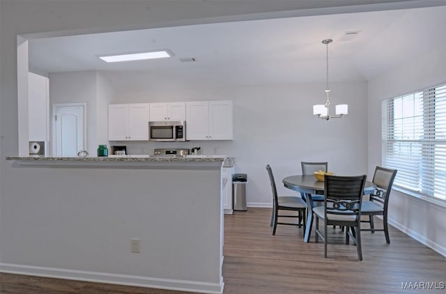 kitchen with a healthy amount of sunlight, an inviting chandelier, lofted ceiling, stainless steel appliances, and white cabinetry