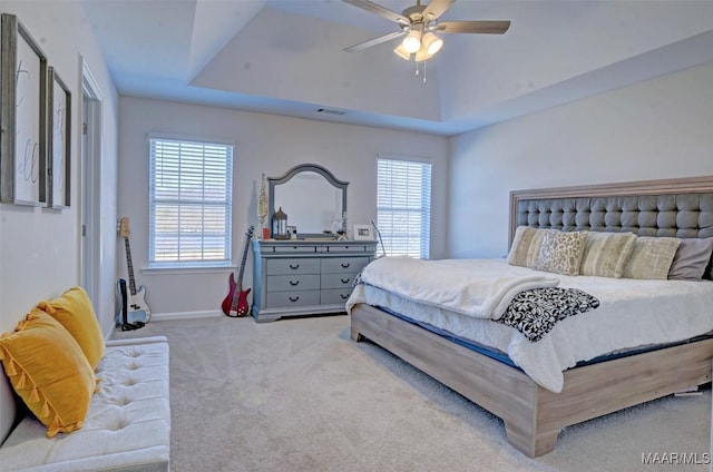 carpeted bedroom featuring a raised ceiling, multiple windows, a ceiling fan, and visible vents