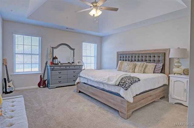 bedroom with visible vents, light colored carpet, a raised ceiling, and ceiling fan