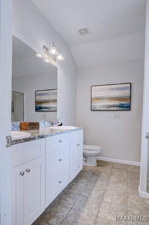 full bath featuring visible vents, double vanity, a sink, vaulted ceiling, and toilet