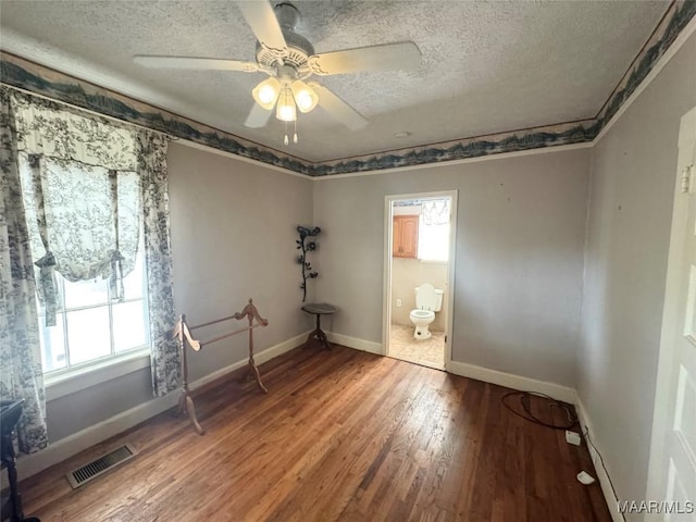 empty room with baseboards, wood finished floors, visible vents, and a textured ceiling