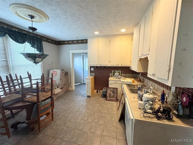 kitchen with a sink, white cabinetry, light countertops, light tile patterned floors, and decorative backsplash