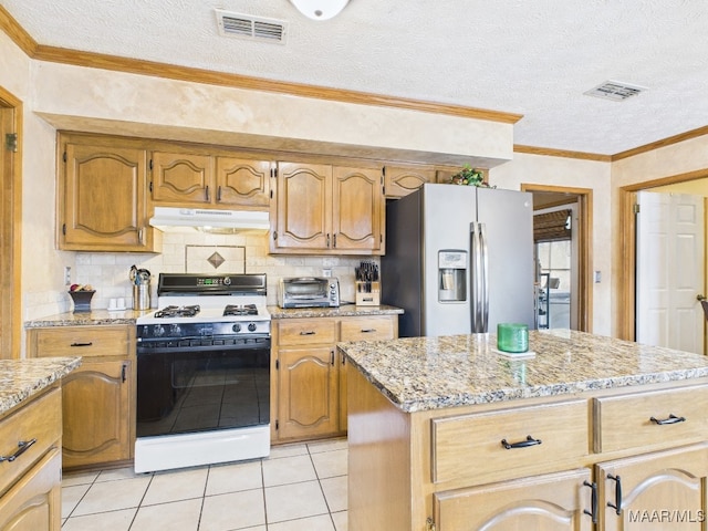 kitchen with visible vents, stainless steel refrigerator with ice dispenser, under cabinet range hood, backsplash, and gas stove