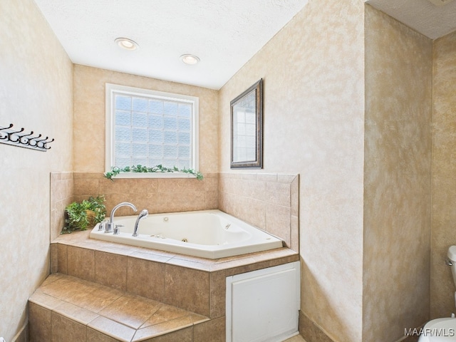 full bath with toilet, a tub with jets, and a textured ceiling