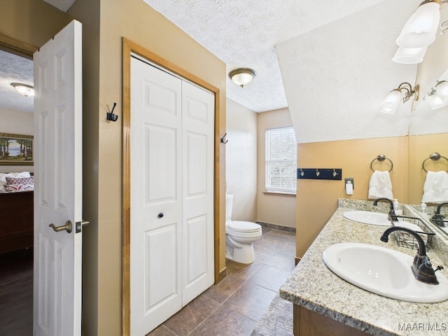 ensuite bathroom with a closet, toilet, a textured ceiling, and a sink