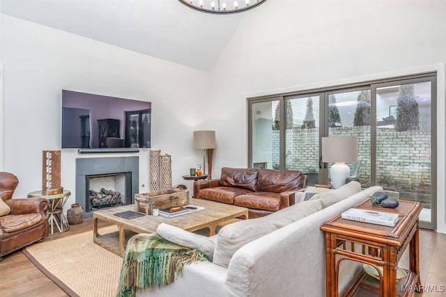 living room featuring a fireplace, high vaulted ceiling, an inviting chandelier, and wood finished floors