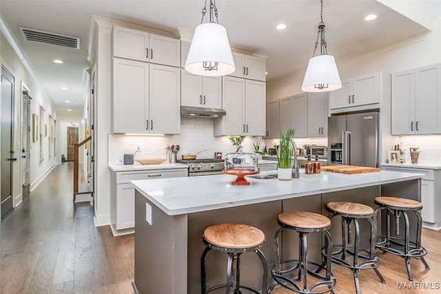 kitchen with visible vents, under cabinet range hood, a center island with sink, wood finished floors, and stainless steel appliances