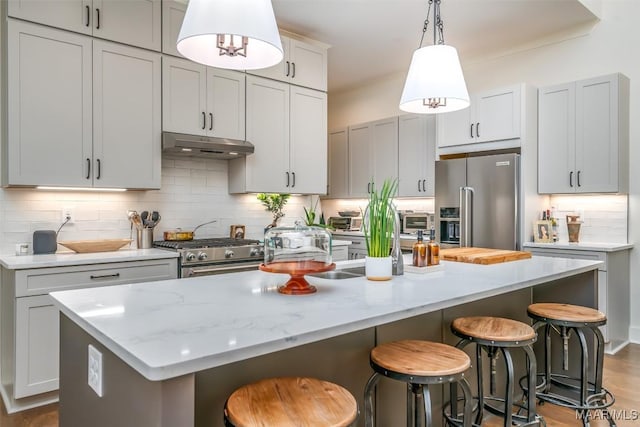 kitchen featuring a breakfast bar, a kitchen island with sink, stainless steel appliances, decorative backsplash, and under cabinet range hood