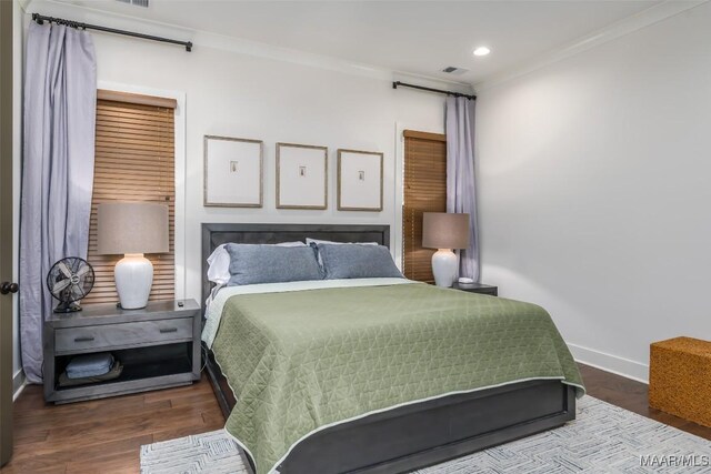 bedroom featuring visible vents, baseboards, wood finished floors, and crown molding