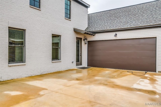 exterior space with an attached garage, brick siding, and roof with shingles