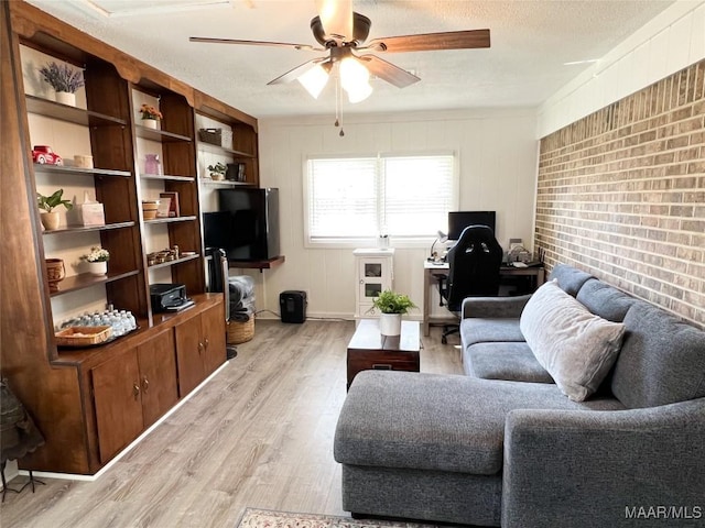 living area featuring brick wall, a textured ceiling, light wood-type flooring, and a ceiling fan