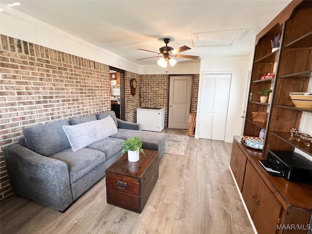 living room with attic access, light wood-style floors, brick wall, and ceiling fan