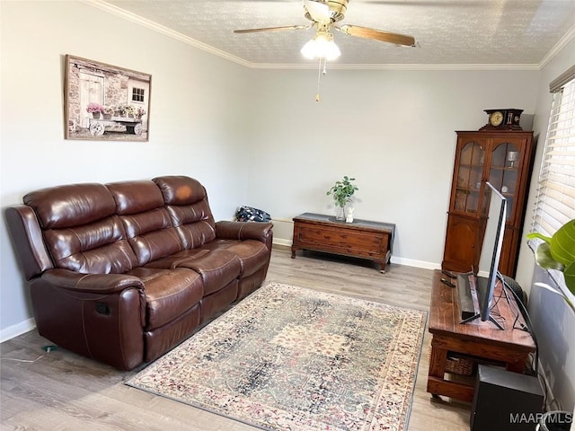 living area with a ceiling fan, baseboards, a textured ceiling, crown molding, and light wood-type flooring