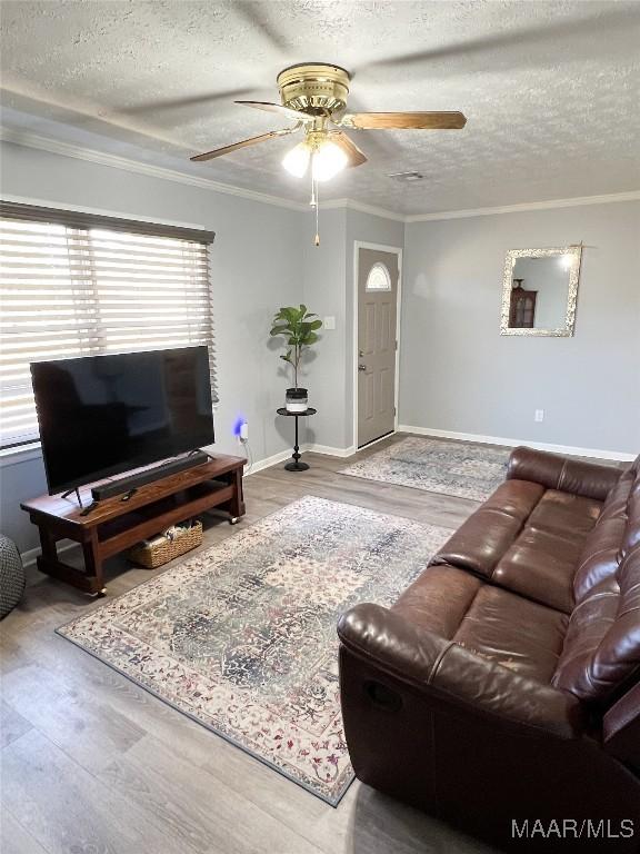 living area with a textured ceiling, wood finished floors, a ceiling fan, and ornamental molding