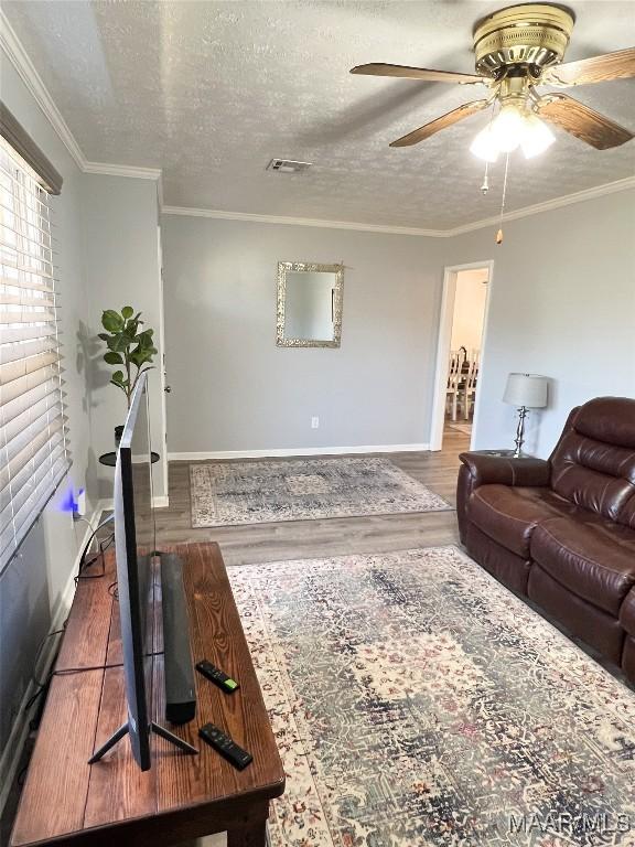 living area with a ceiling fan, wood finished floors, visible vents, a textured ceiling, and crown molding