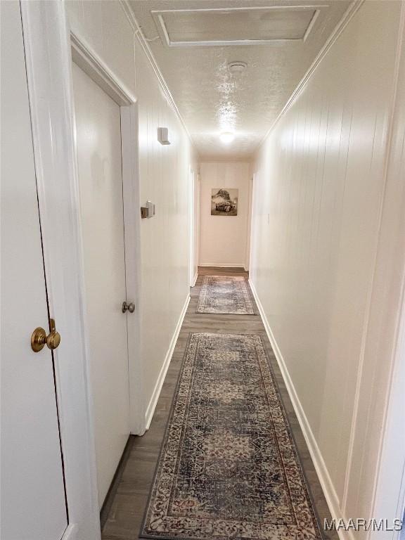 hallway with crown molding, baseboards, attic access, dark wood-style floors, and a textured ceiling