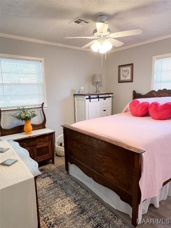 bedroom with ceiling fan, crown molding, visible vents, and a textured ceiling