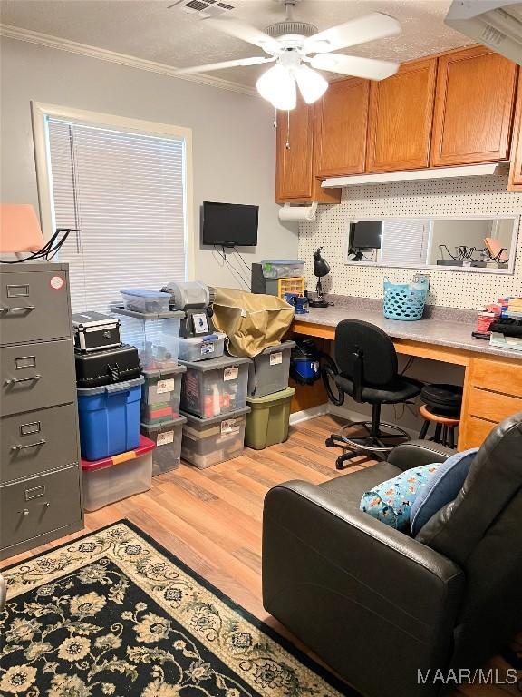 office area featuring a ceiling fan, wood finished floors, visible vents, built in study area, and crown molding