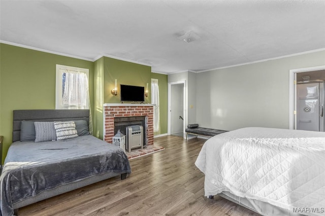 bedroom featuring a brick fireplace, wood finished floors, baseboards, and ornamental molding