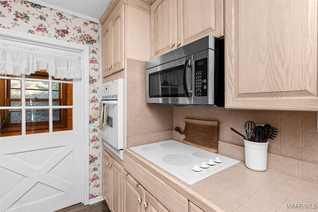 kitchen featuring white appliances, wallpapered walls, light brown cabinetry, tile counters, and backsplash