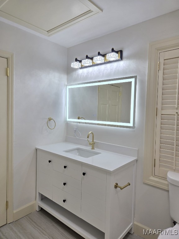 bathroom with toilet, vanity, baseboards, and wood finished floors