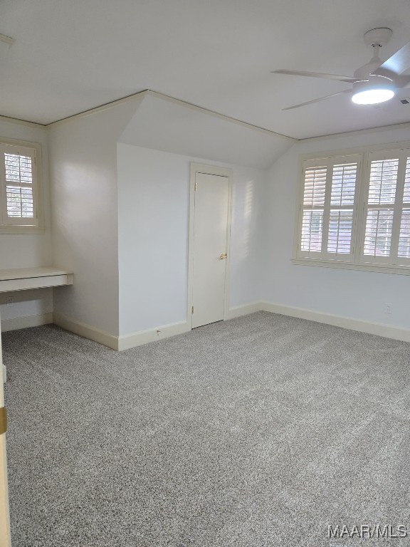 carpeted spare room featuring baseboards, lofted ceiling, and ceiling fan